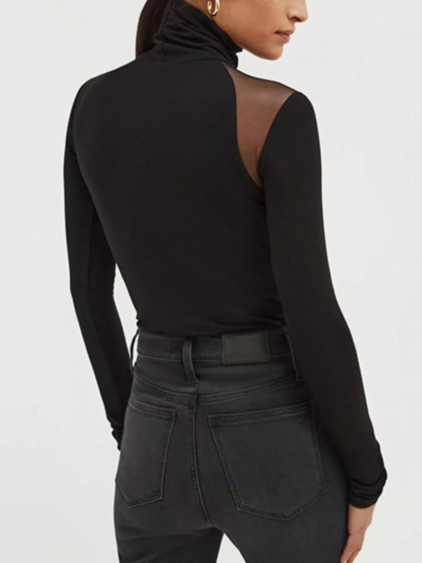 Back view of a black Mesh Shoulder Turtleneck Bodysuit with sheer mesh details, styled with high-waisted jeans.