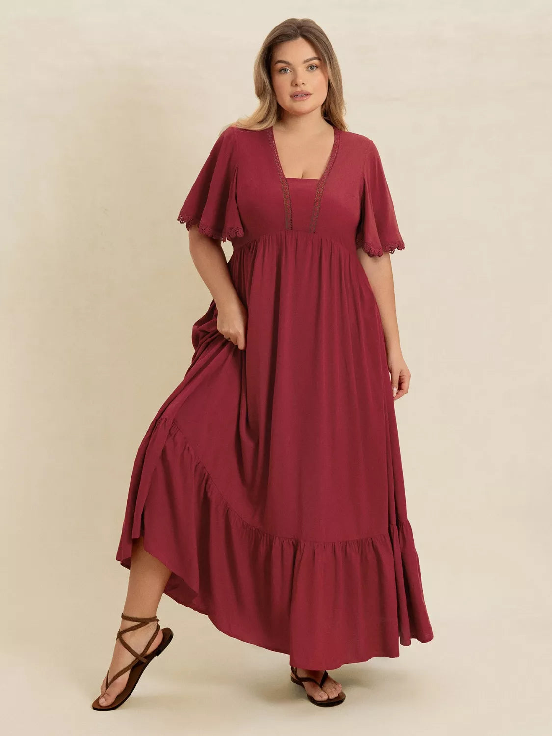 Plus Size Lace Detail Flutter Sleeve Maxi Dress model wearing a burgundy flowing dress with lace accents and flutter sleeves.