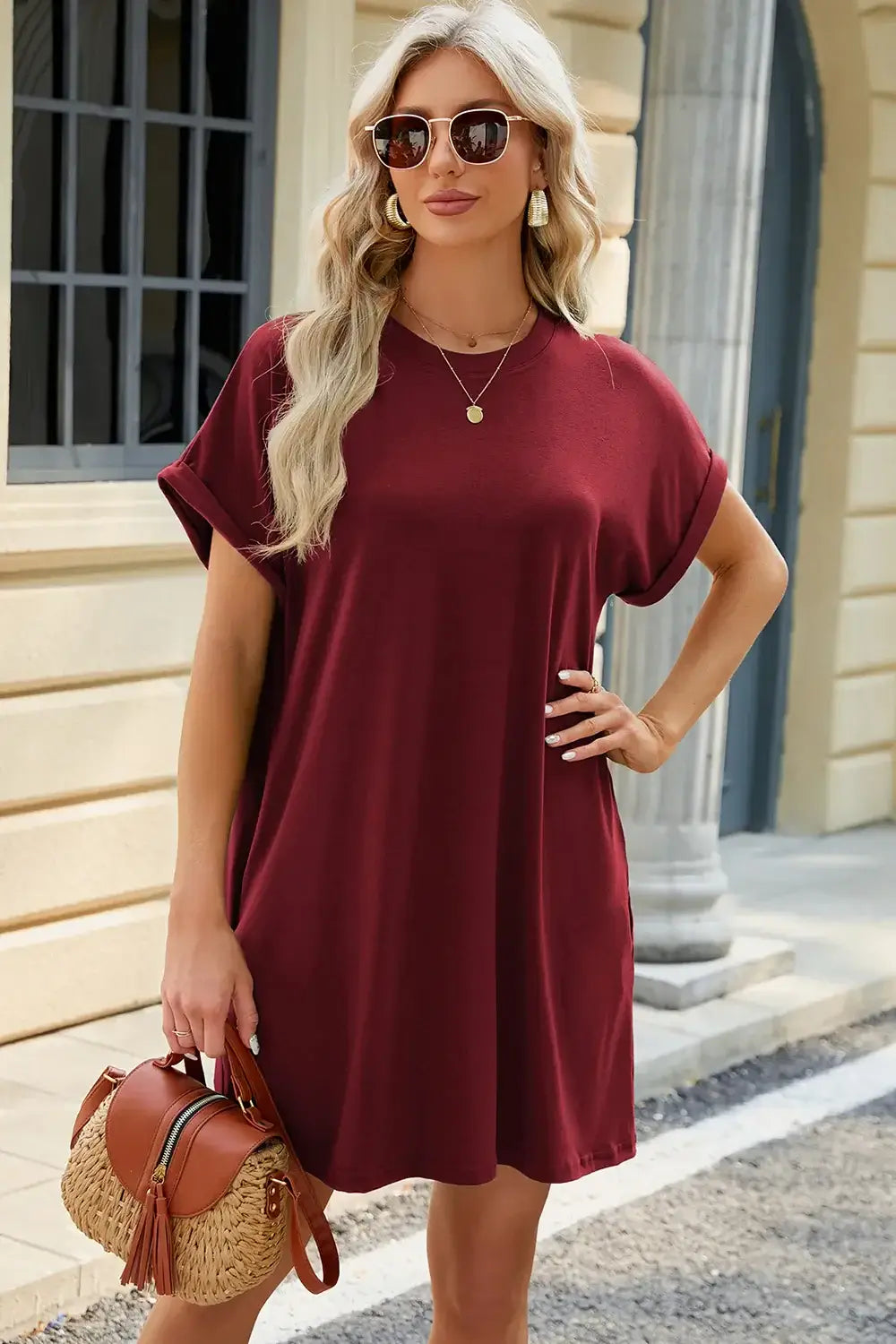 Stylish woman wearing a maroon round neck rolled short sleeve tee dress, accessorized with sunglasses and a bag.