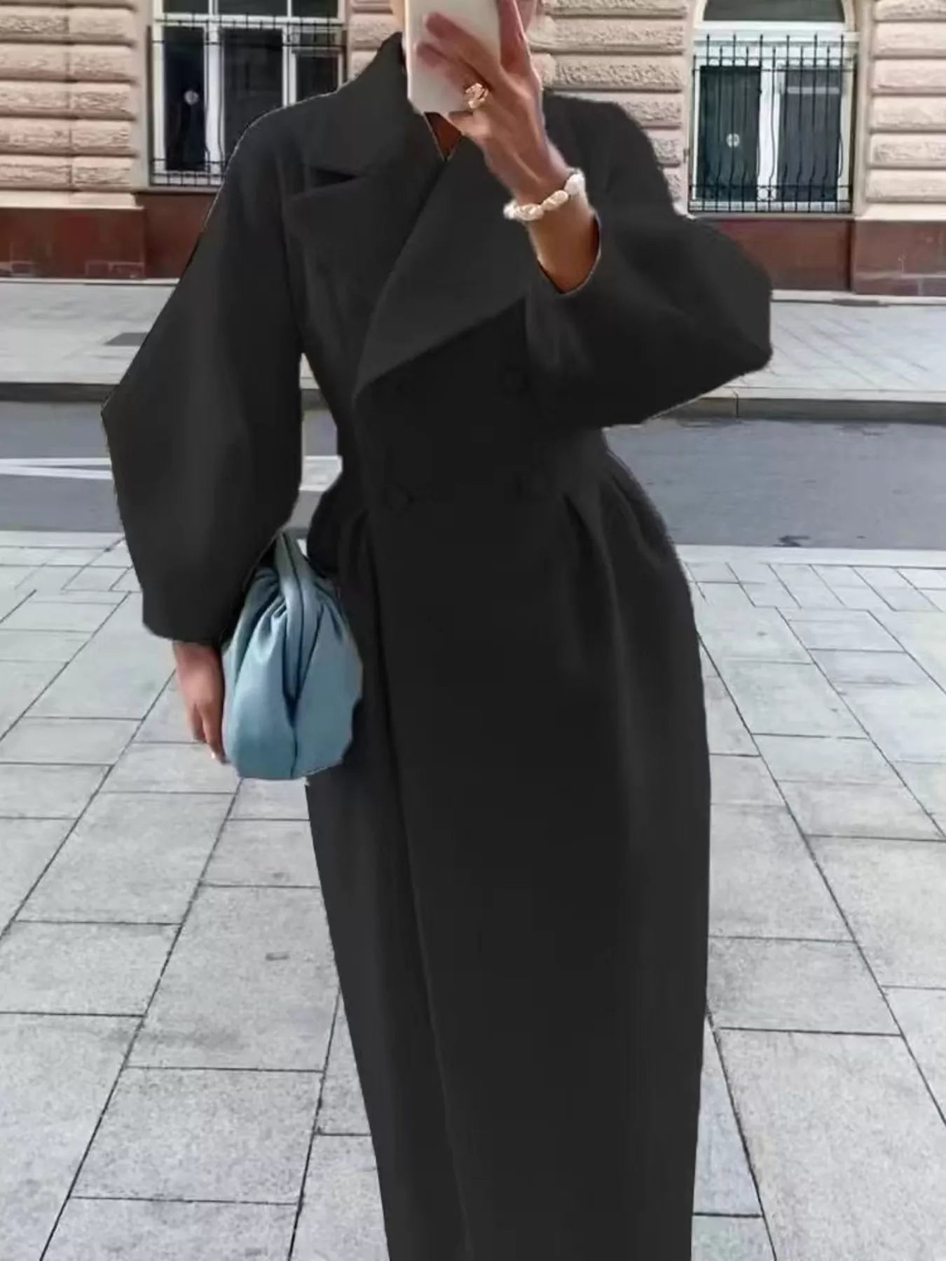Double-Breasted Longline Coat with elegant tailored silhouette, styled with a light blue handbag on a city street.