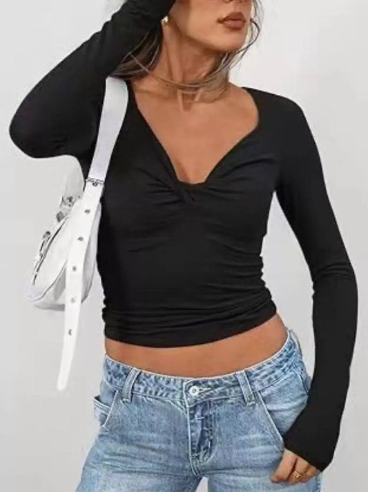 Woman wearing black long sleeve fitted t-shirt with twist front design and high-waisted jeans, styled with a chic handbag.