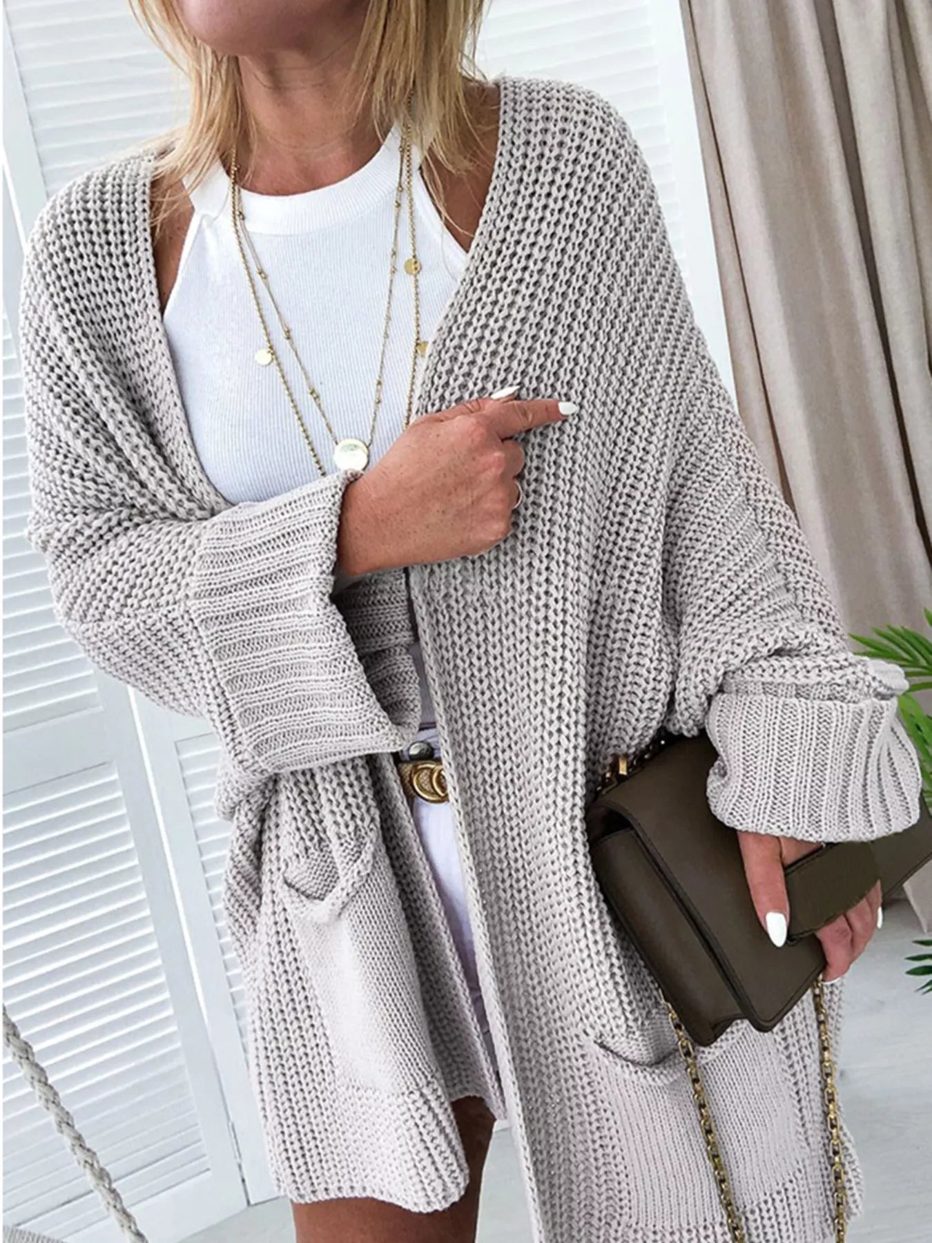 Woman wearing an Oversized Fold Over Sleeve Open Front Cardigan in beige, styled with a white dress and accessories.