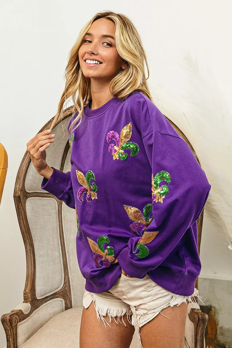 BiBi Fleur De Lis Sequin Patches Mardi Gras Sweatshirt worn by a smiling woman in a vibrant purple color with sequined patches.