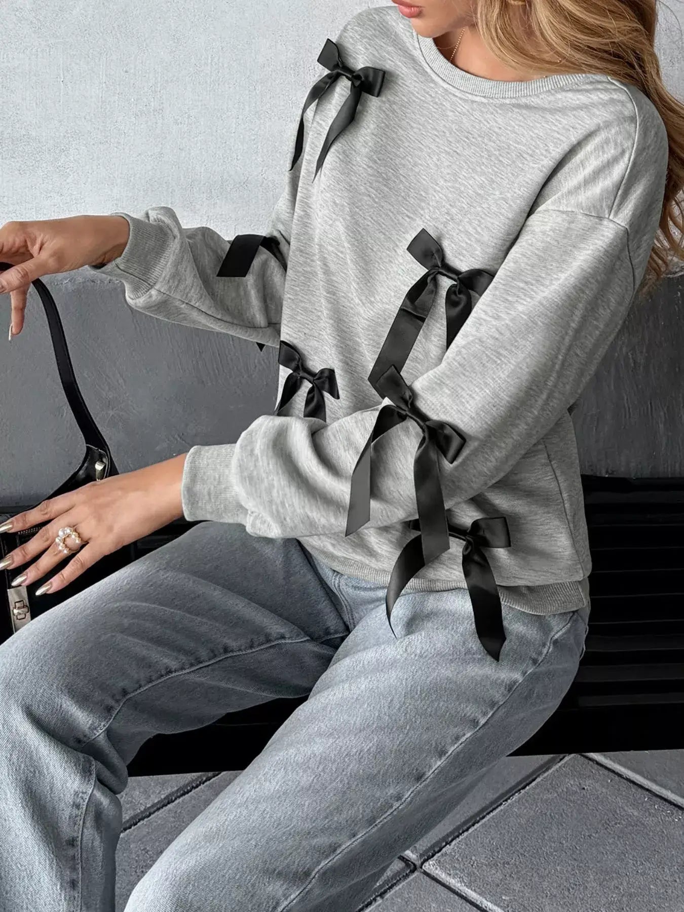 Model wearing a Bow Detail Round Neck Sweatshirt with side bows, paired with jeans, showcasing a casual yet stylish look.