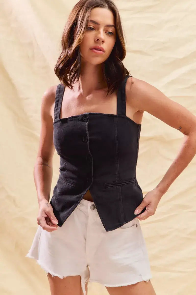 Model wearing a fitted black denim sleeveless top with button details and white denim shorts against a neutral backdrop.