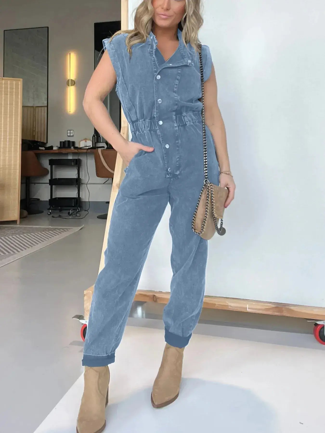 Woman wearing a full size button front cap sleeve denim jumpsuit, styled with a handbag and ankle boots.