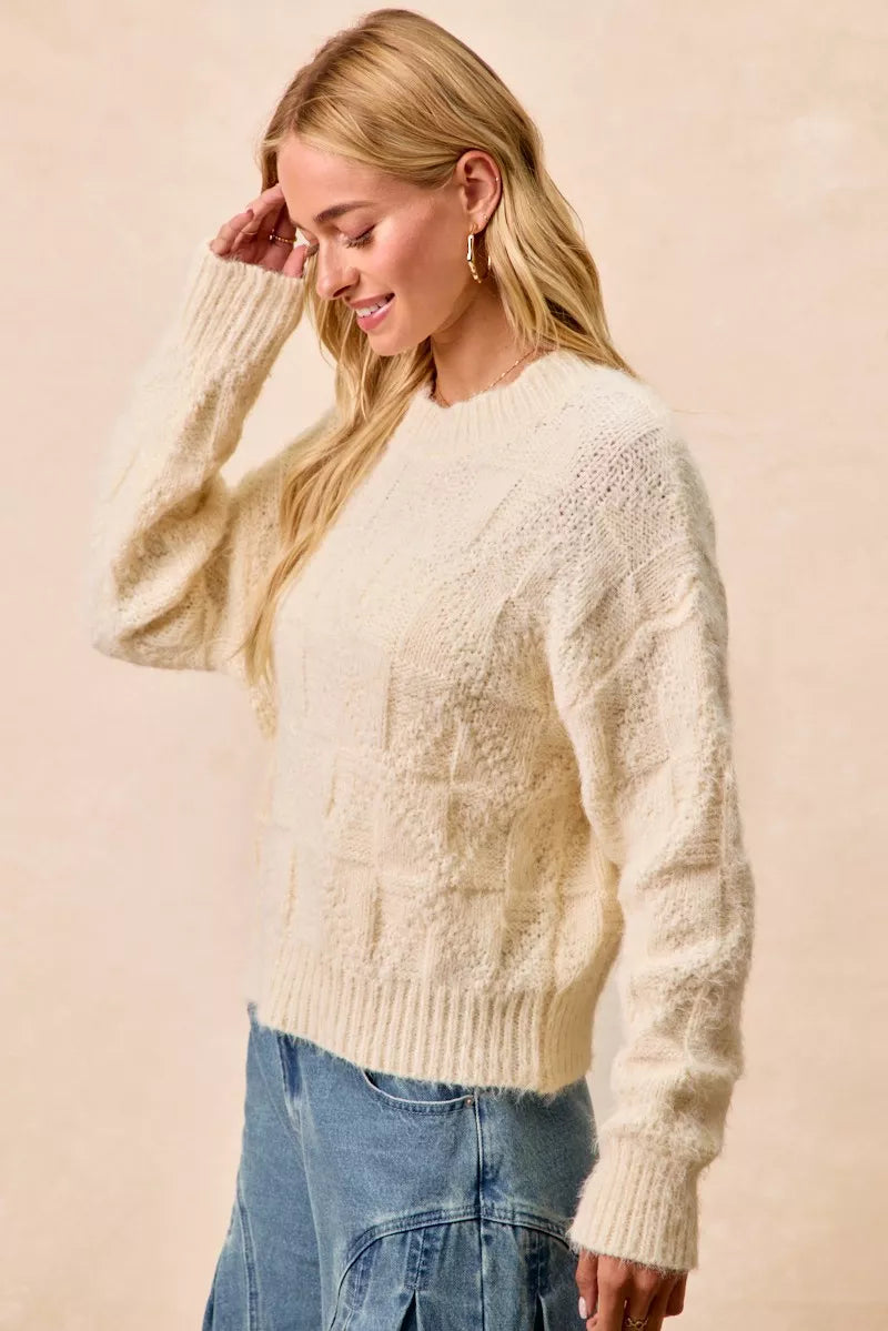 Woman wearing the BiBi Checker Board Drop Shoulder Sweater in cream, showcasing a stylish and relaxed fit.