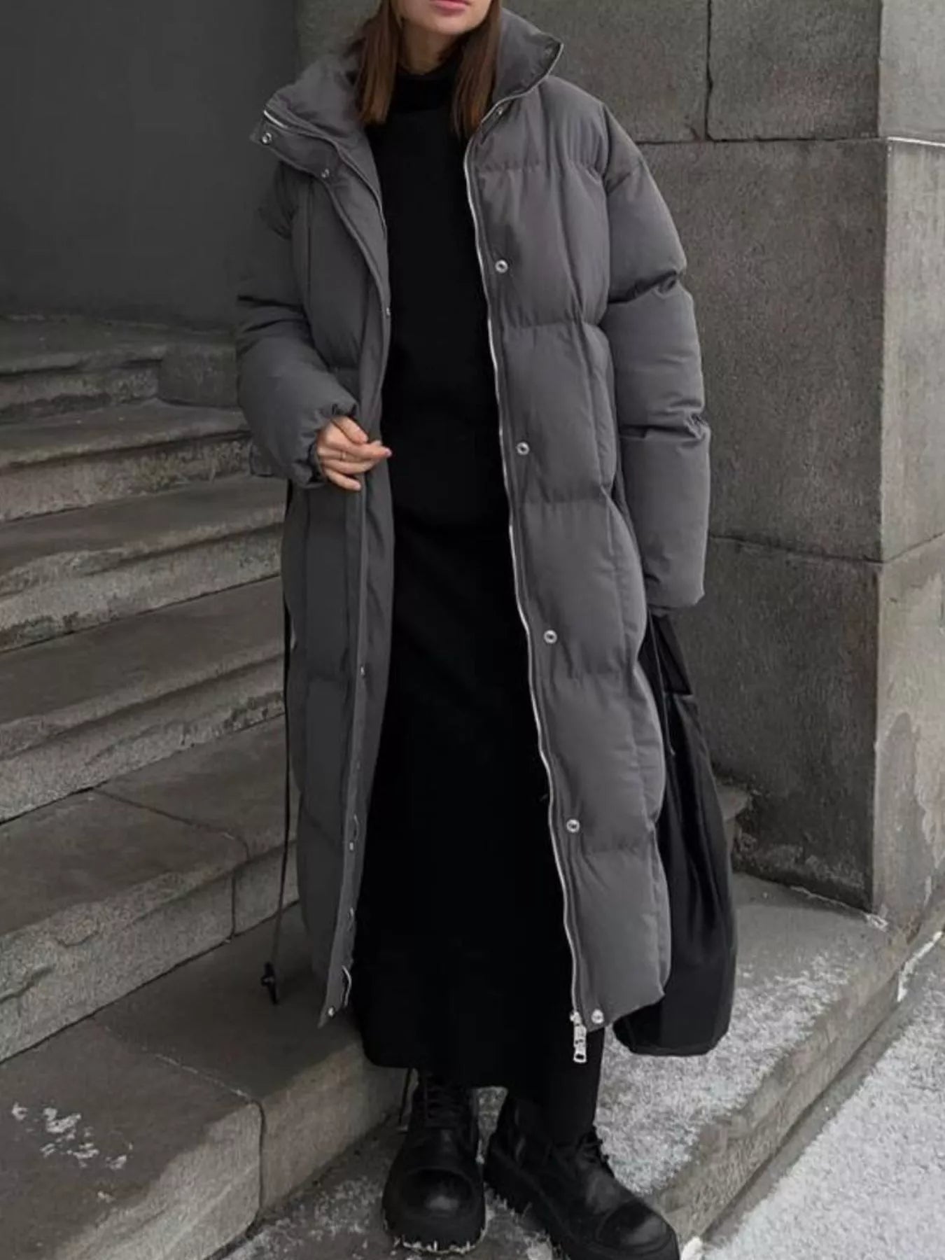 Longline Padded Winter Coat Belted warm women jacket in gray worn by a model standing on stone steps.