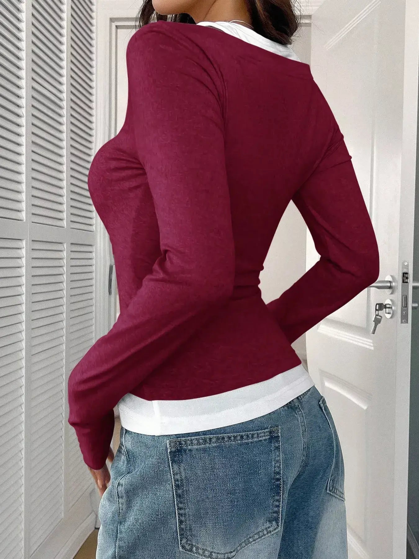 Woman wearing a burgundy scoop neck long sleeve t-shirt with a white collar, styling it casually with light blue jeans.