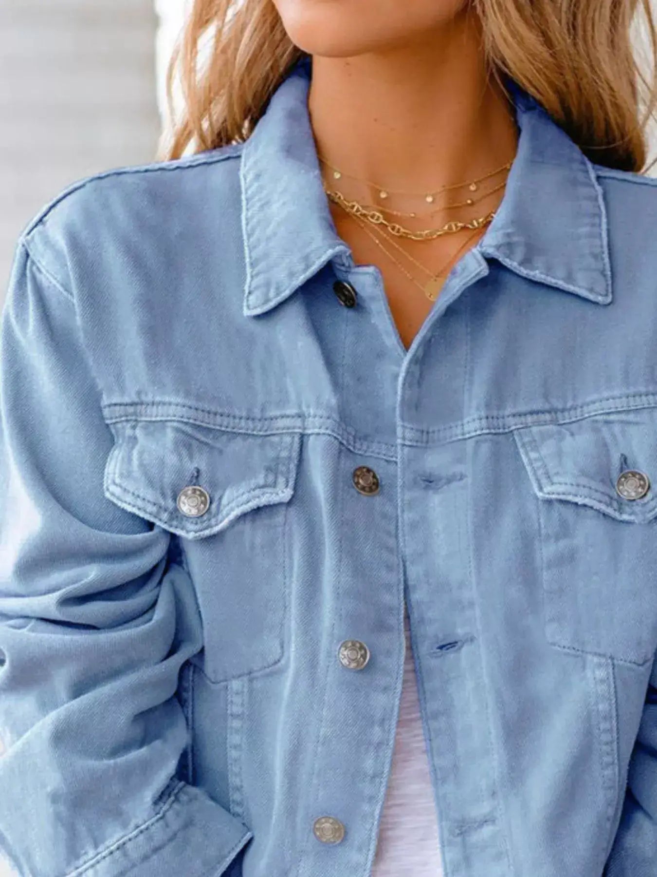Close-up of a woman wearing a light blue button-up long sleeve denim jacket with layered necklaces.