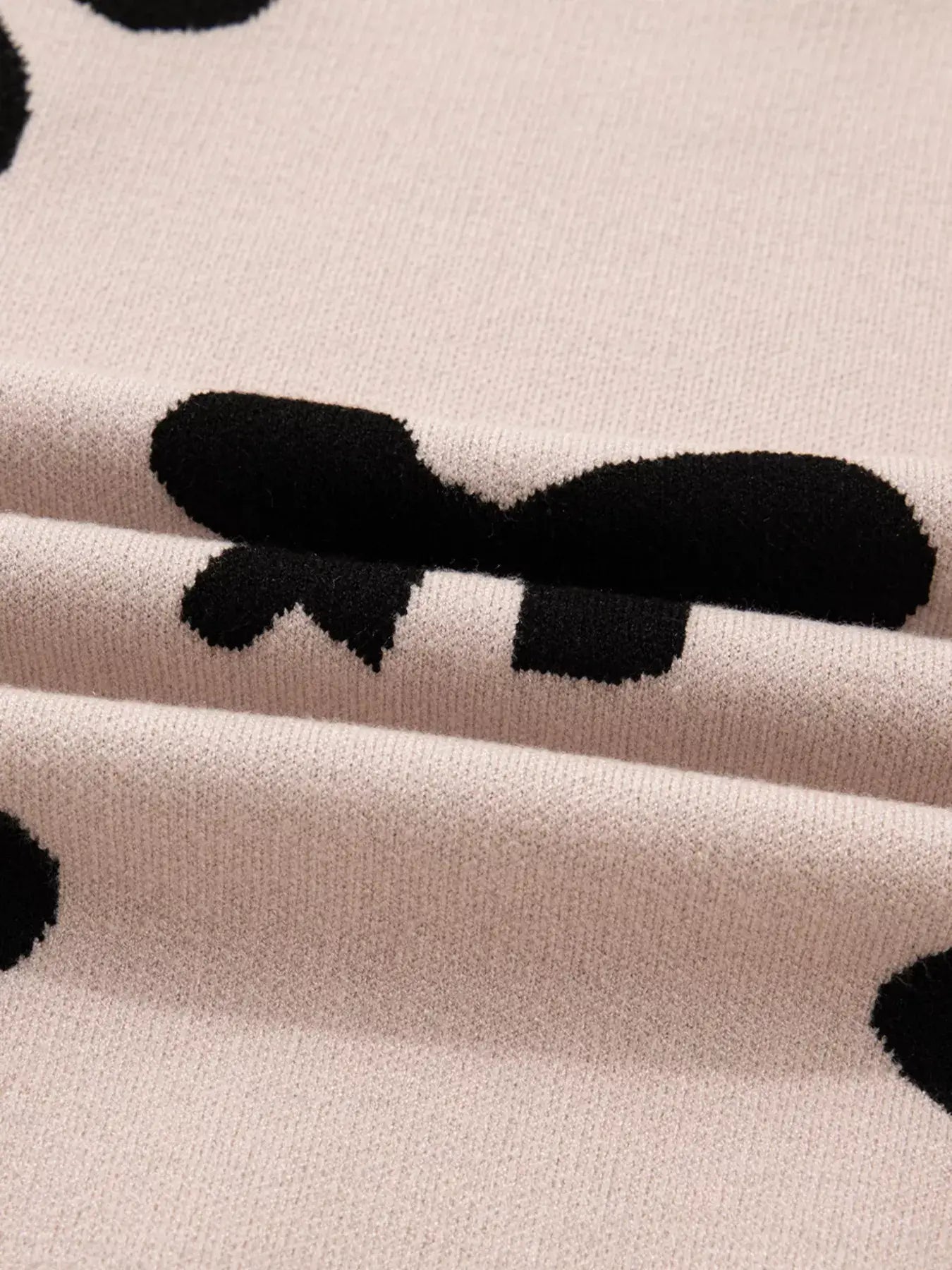 Close-up of the fabric texture featuring bow pattern on the pearl embellished bow pattern loose sweater.
