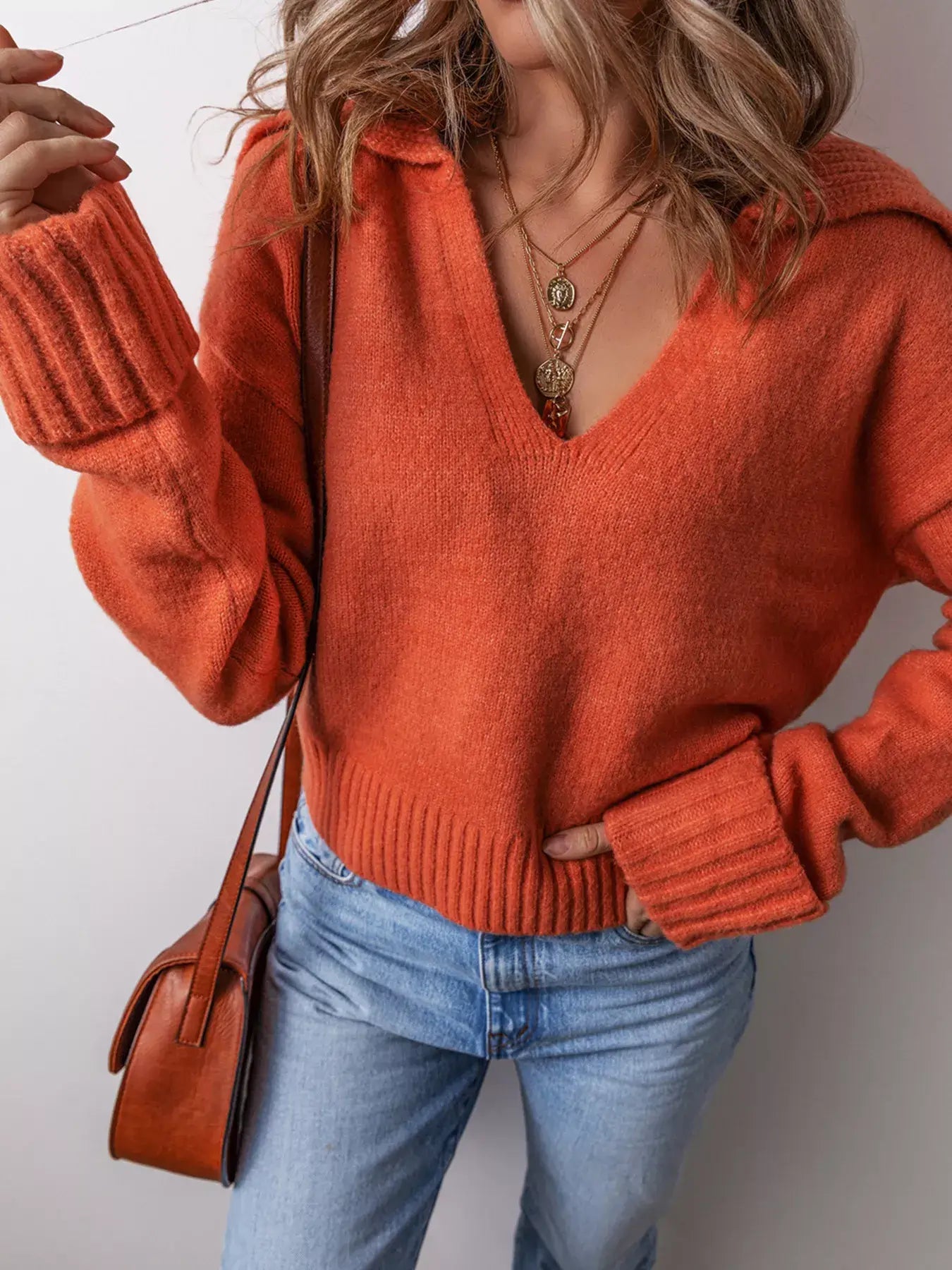 A model wearing a collared v neck ribbed edge sweater in orange, showcasing its soft knit design and flattering V-cut.