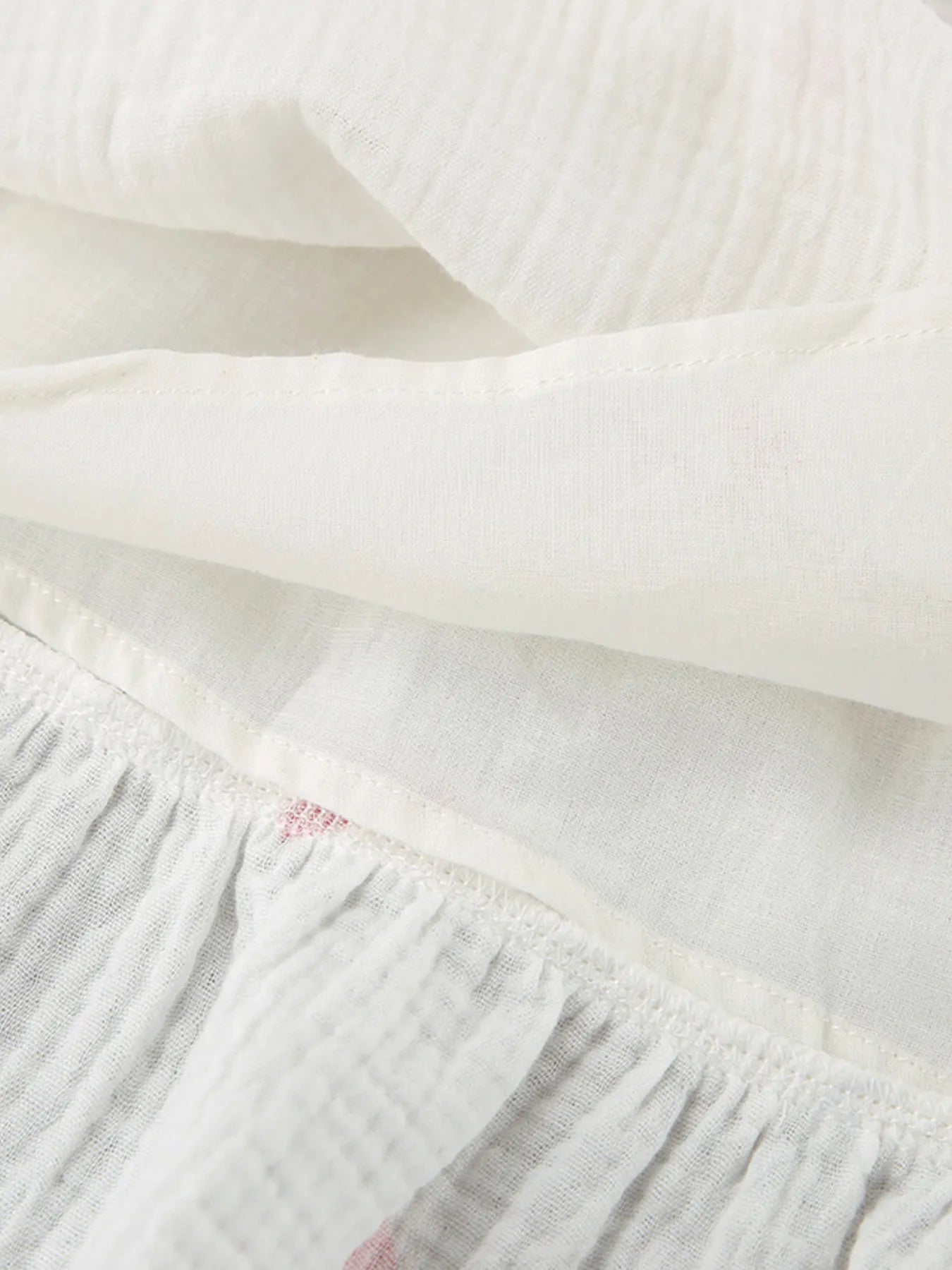 Close-up view of fabric texture showcasing the Heart Printed Off-Shoulder Ruffle Mini Dress in white with ruffle detailing.