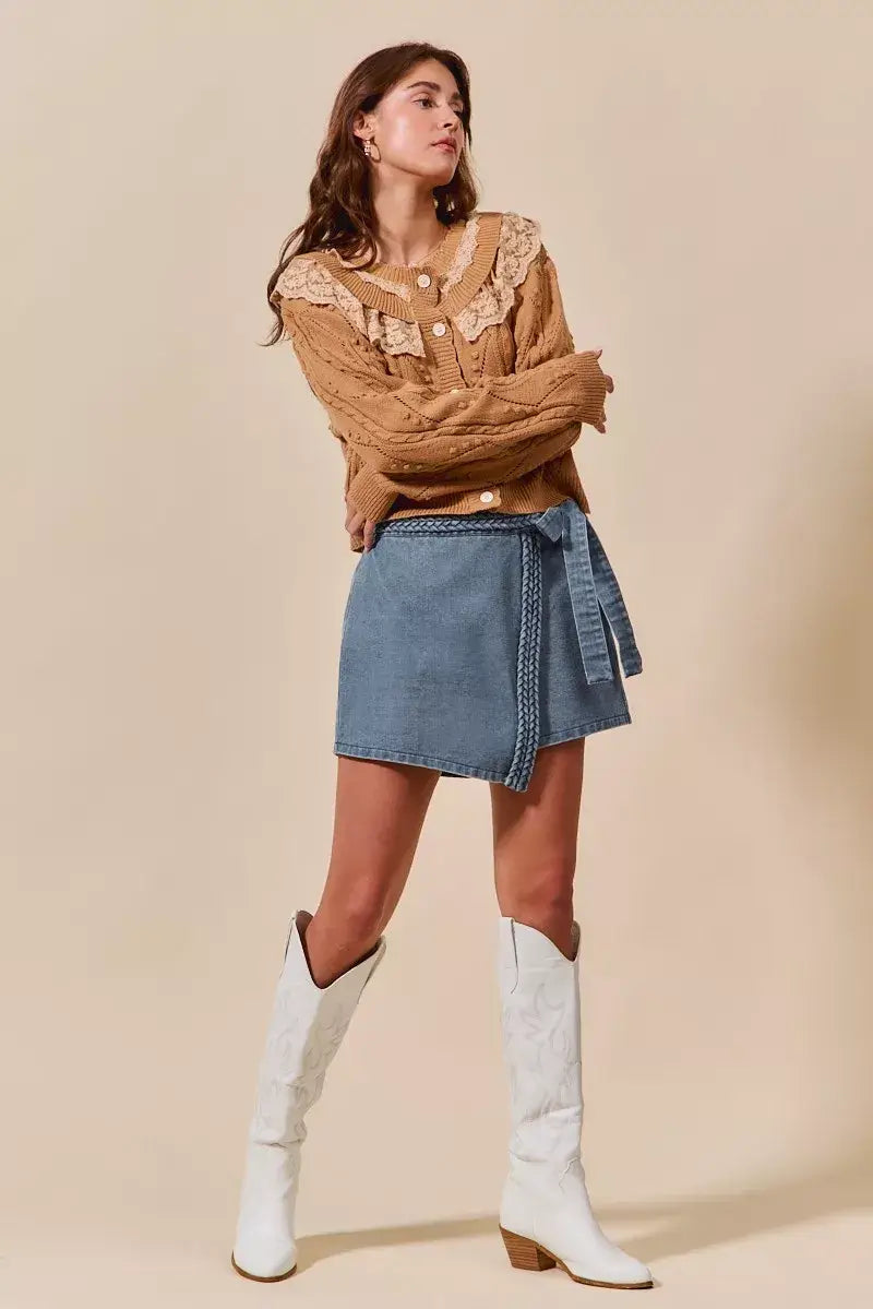 Woman in a wrap braided trimmed denim skort, paired with a brown blouse and white cowboy boots.